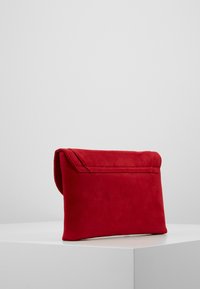 Pochette en daim rouge avec un dessus plié et des coutures surpiquées, présentant une texture lisse et un design simple. Forme rectangulaire, sans matériel métallique.