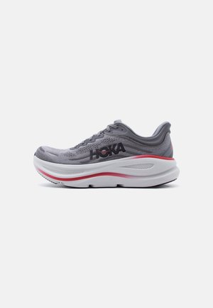 Grå løbesko med tyk hvid og rød sål, sort "HOKA" logo på siden og polstret hælkappe på hvid baggrund.