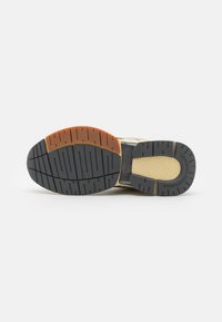 Suola della scarpa con una base in gomma nera, sezioni grigie e arancioni, testurizzata per la presa e un design a motivo per la trazione.