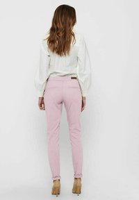 Pantalons ajustés rose clair en mélange de coton, avec des poches arrière et des ourlets roulés, associés à un blouse blanche.