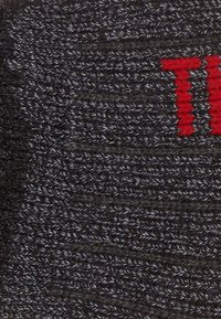 Gorro de punto en gris oscuro con una textura sutil; presenta un logo rojo bordado en la parte delantera.