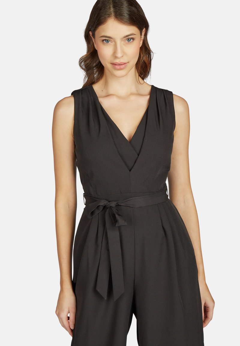 Schwarzer ärmelloser Jumpsuit mit tiefem V-Ausschnitt, plissiertem Design und einem gebundenen Taillenkorb. Glattes Material mit matter Oberfläche.
