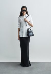 Άσπρο πουκάμισο με γιακά και μακριά μανίκια συνδυασμένο με μαύρη φούστα μήκους μέχρι το πάτωμα. Αξεσουάρ περιλαμβάνουν μια μικρή μαύρη τσάντα χειρός και σκούρα γυαλιά ηλίου.