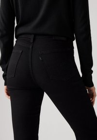 Jeans de denim negro con un diseño ajustado, que cuentan con dos bolsillos traseros y costuras sutiles. La tela tiene una textura suave y color sólido.
