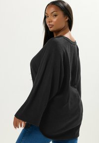 Schwarzer, übergroßer gerippter Pullover mit weiten Ärmeln, rundem Ausschnitt und strukturiertem Stoff, kombiniert mit blauen Jeans.