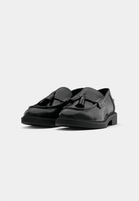 Black leather loafers featuring a broad strap and tassel detail, with a flat sole and smooth finish. Suitable for casual or formal occasions.