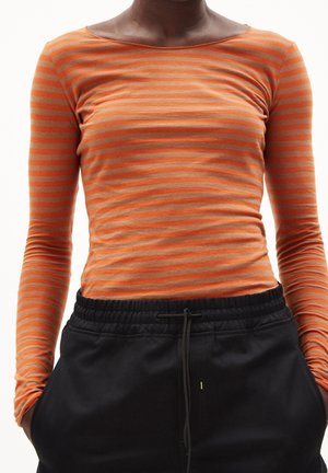 Camiseta de manga larga con rayas naranjas y grises, hecha de tela suave. Presenta un escote amplio y mangas ajustadas, combinada con pantalones negros con cordón.