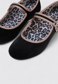 Bailarinas de terciopelo negro con punta redonda, ribete beige y plantilla de animal print. Presentan una hebilla decorativa en la correa.