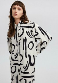 Camicia button-up in tessuto crema con audaci motivi astratti neri, vestibilità rilassata con spalle scese e un classico design del colletto.
