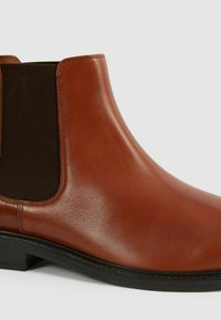 Stivale Chelsea in pelle marrone con pannelli elasticizzati sui lati, finitura testurizzata e punta rotonda. Suola in gomma nera con una leggera elevazione del tacco.