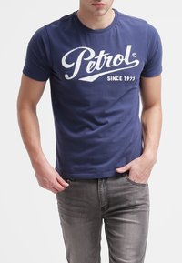 Tmavě modré bavlněné tričko s velkým bílým logem "Petrol" s nápisem "since 1973" pod ním. Krátké rukávy a klasický kulatý výstřih.