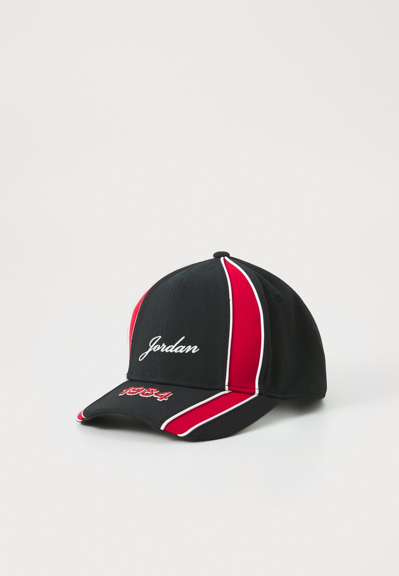 Juodas beisbolo kepurė su raudonomis ir baltomis juostelėmis, išsiuvinėtas žodis "Jordan" priekyje ir "1984" ant vizoriaus. Pagaminta iš tekstūruoto audinio.