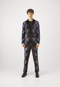 Svart dress med fargerikt sommerfugl mønster i blått, rødt og oransje. Sateng tekstur, tradisjonell krage og figursydd design, kombinert med svarte sko.