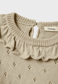 Pull en tricot beige avec un col à volants, une fermeture au dos en forme de clé et de petits motifs décoratifs sur le tissu. Étiquette de la marque visible.