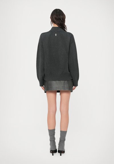 Camisola de malha cinzenta carvão com gola alta, mangas raglan e punhos canelados, combinada com uma saia curta de couro preta e meias cinzentas.