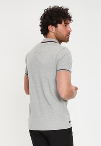 Grå polo-shirt med korte ærmer, med burgundy kant på kraven og ærmeafslutningerne. Glat struktur, moderne pasform og logo-detalje på siden.