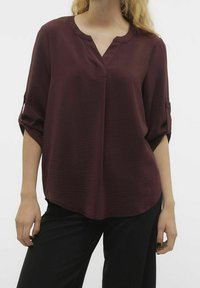 Blusa bordeaux a maniche corte con un tessuto morbido e texture, dotata di scollatura a V e maniche arrotolate, abbinata a pantaloni neri.