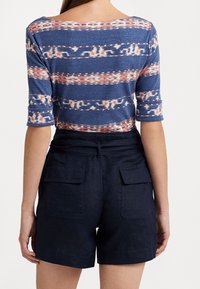 Top de mezcla de algodón con un patrón de rayas azules y coral, de mangas tres cuartos. Combinado con pantalones cortos de talle alto en un azul marino oscuro con bolsillos.