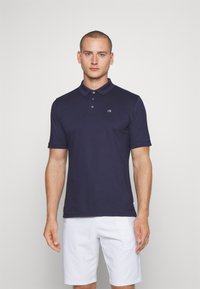 Navy blue polo shirt in a cotton blend, featuring a three-button placket and short sleeves. Small embroidered logo on the chest.