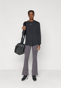 Μαύρη μπλούζα Nike με μακριά μανίκια, γκρι φαρδιά κολάν, μαύρα αθλητικά παπούτσια και μαύρη τσάντα ώμου με ρυθμιζόμενο λουρί και φερμουάρ.