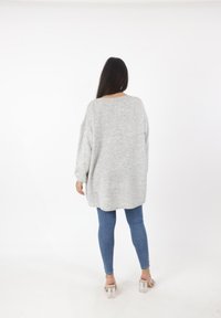 Overmaatse grijze gebreide trui met drop shoulders, ronde halslijn en geribbelde details, gecombineerd met strakke blauwe jeans en doorzichtige blokhak schoenen.