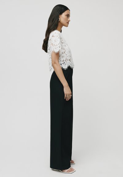 Witte kanten cropped top met franjes aan de mouwen, gecombineerd met high-waisted zwarte broek. Glad materiaal en strakke pasvorm. Geen zichtbare patronen.