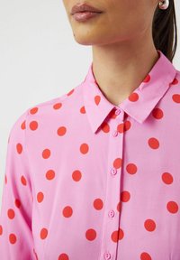 Rosa skjorte med knapper som har røde prikker, krage-design, myk stoffkvalitet og knapper som matcher skjortefargen.