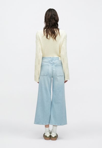 Φαρδιά τζιν σε ανοιχτό γαλάζιο με ψηλή μέση, συνδυασμένα με εκρού χοντρή πλεγμένη ζακέτα με ριμπ και πλεκτά σχέδια.