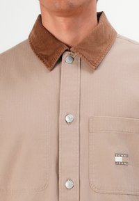 Beige button-up shirt with brown corduroy collar and a front pocket featuring a Tommy Jeans logo patch.