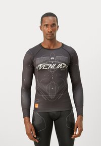 Czarna rash guard z długim rękawem z białym graficznym wzorem, który zawiera logo, okrągłe wzory oraz akcenty na rękawach i pasie.