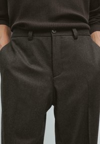 Man wearing dark brown ribbed sweater tucked into high-waisted dark gray wool trousers with button and belt loops.