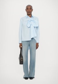Ljusblå skjorta med ett stort rosett-detajl, matchad med utsvängda ljusdenimjeans. Svart väska framhäver outfiten.