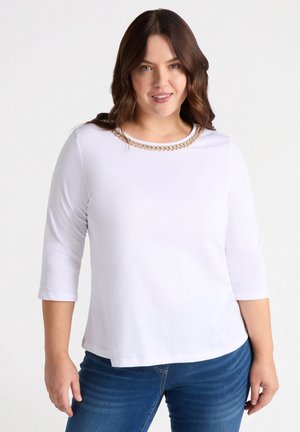Blusa blanca de mangas tres cuartos con un escote redondo adornado con un detalle dorado en forma de cadena. Tela suave con un corte holgado.