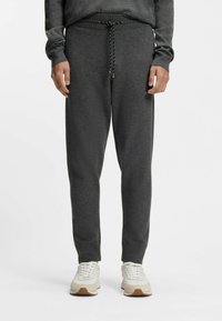 Ciemnoszare spodnie dresowe z sznurkiem w pasie, ściągaczami przy nogawkach i miękką tkaniną, w połączeniu z kremowobiałymi butami sportowymi.