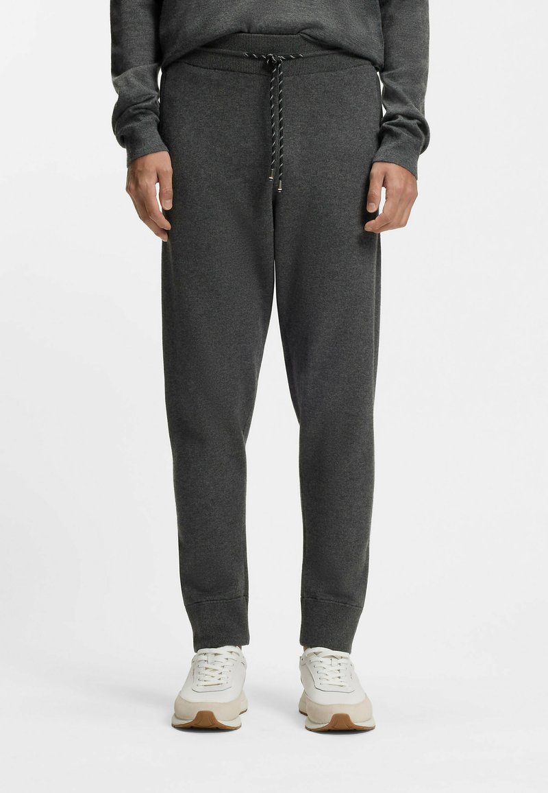 Ciemnoszare spodnie dresowe z sznurkiem w pasie, ściągaczami przy nogawkach i miękką tkaniną, w połączeniu z kremowobiałymi butami sportowymi.