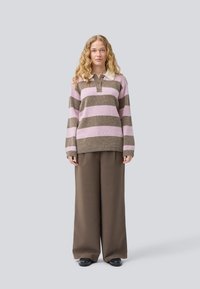 Maglione a righe in rosa e marrone con colletto, tre bottoni e orlo a coste, abbinato a pantaloni larghi marroni e scarpe nere.