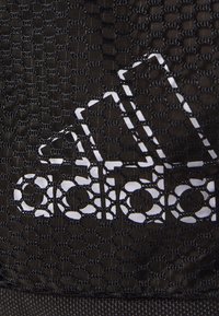 Černá síťovina vyniká výrazným bílým logem Adidas, které se skládá ze tří diagonálních pruhů. Textura je tkaná a má mřížkový vzor.