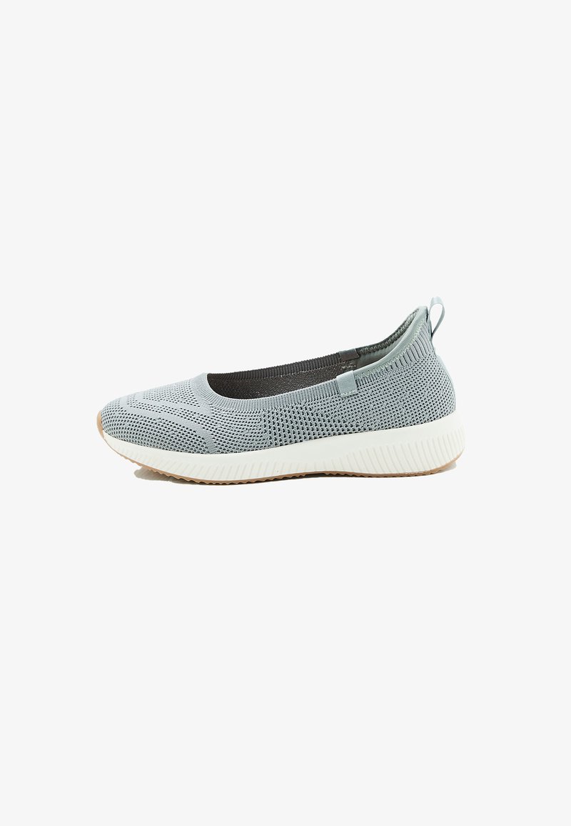 Lichtgrijze gebreide slip-on sneaker met witte getextureerde zool en treklusje aan de hiel, vanuit de zijkant getoond op een witte achtergrond.