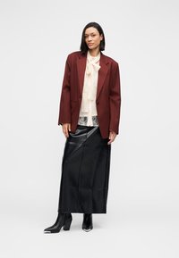 Bordeauxrood colbert over een kanten blouse, gecombineerd met een zwarte leren maxirok en strakke zwarte enkellaarsjes met zilveren accenten.