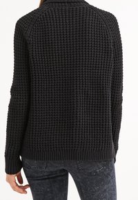 Schwarzer Strickpullover mit strukturiertem Muster, hochgeschlossenem Kragen und gerippten Bündchen und Saum, von hinten betrachtet.