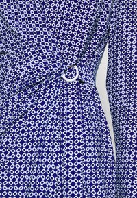 Abito blu con motivo geometrico bianco, design avvolgente e un accento ad anello bianco in vita. Tessuto morbido al tatto.