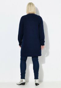 Marinblå långärmad stickad tröja, midja-höjd, i kombination med mörkblå jeans och silverfärgade ankelskor med klack.