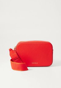 Červená kožená kabelka přes rameno s texturovaným povrchem, zipovým zapínáním a odnímatelným ramenním popruhem. Zlaté logo na přední straně.