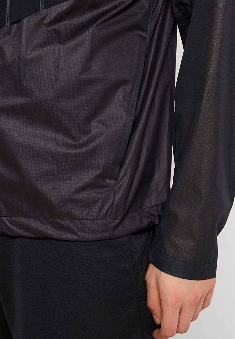 Zwarte lichtgewicht jas met een gladde, licht glanzende textuur. Heeft een gelaagd ontwerp, zijslits en subtiele reflecterende details.