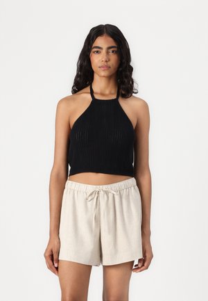 Top corto de halter negro acanalado combinado con pantalones cortos de lino beige. El top presenta un diseño ajustado y un cuello alto, mientras que los pantalones cortos tienen una cintura elástica.
