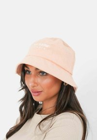 Perzikenkleurige bucket hat gemaakt van zachte, gestructureerde stof, met een brede rand en een geborduurd logo aan de voorkant. Eenvoudig, casual ontwerp.