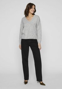 Hallitusest hall kudum V-kaelusega, vabalt langev ja pikkade varrukatega, koos sirgete mustade pükste ja terava ninaga kontsakingadega.