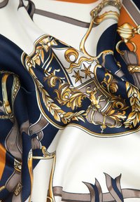 Foulard en soie présentant un motif détaillé avec des motifs dorés complexes sur fond bleu marine et crème. Texture lisse avec un tissu fluide.