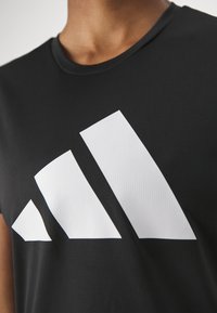 MustBlacki sportpusa, millel on silmapaistev valge geomeetriline logo. Kanga pinnal on tekstuuriline muster ning ümar kaelus.