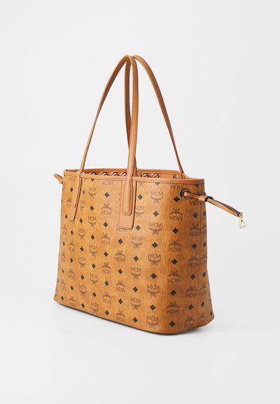 Tan leather tote bag with MCM logo pattern, double shoulder straps, and a drawstring closure on one side, shown on a white background.